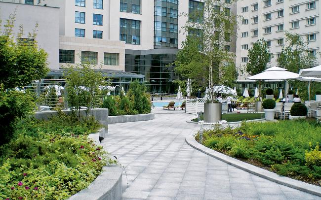 Curved walkways, plant beds and swimming pool surrounded by parasols and sun beds